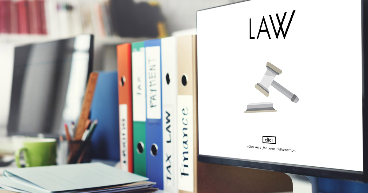 Law office desktop with colorful binders, computer screen showing gavel icon, and green coffee mug