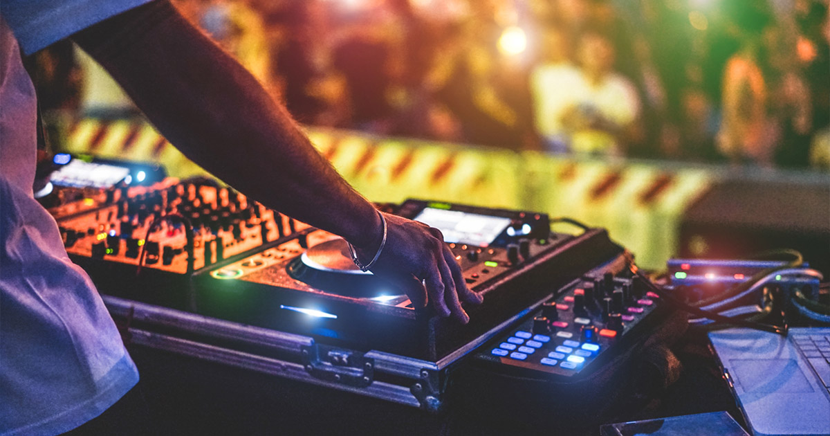 DJ mixing music on professional controller with colorful nightclub lights in background