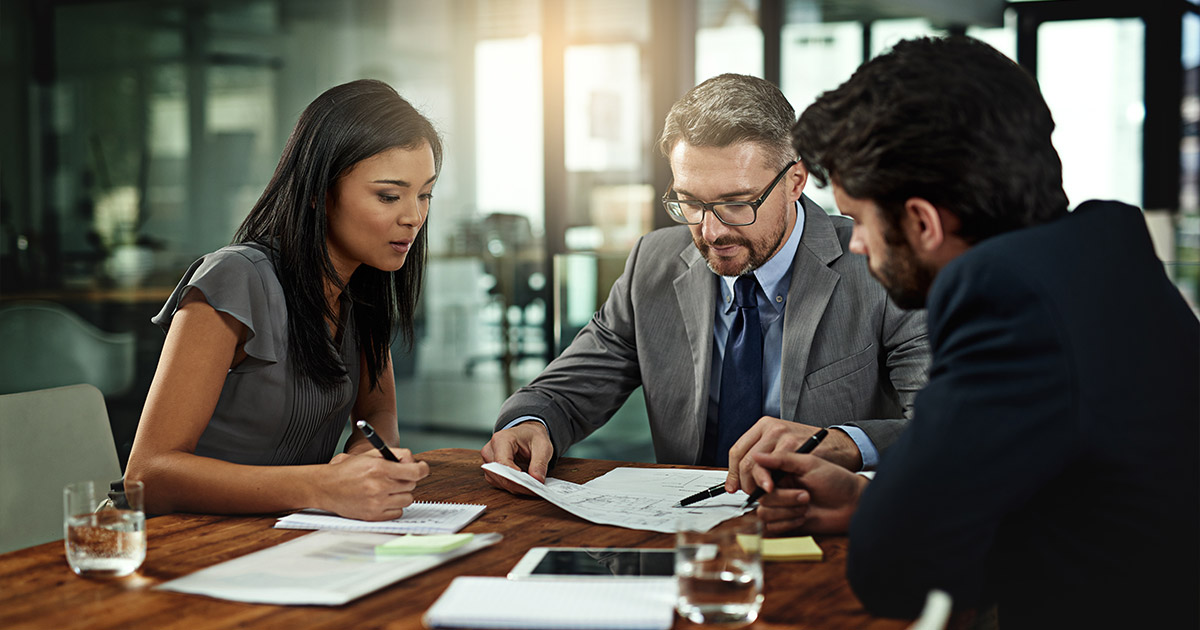 Business meeting with diverse team reviewing documents at wooden conference table, collaborative professional setting