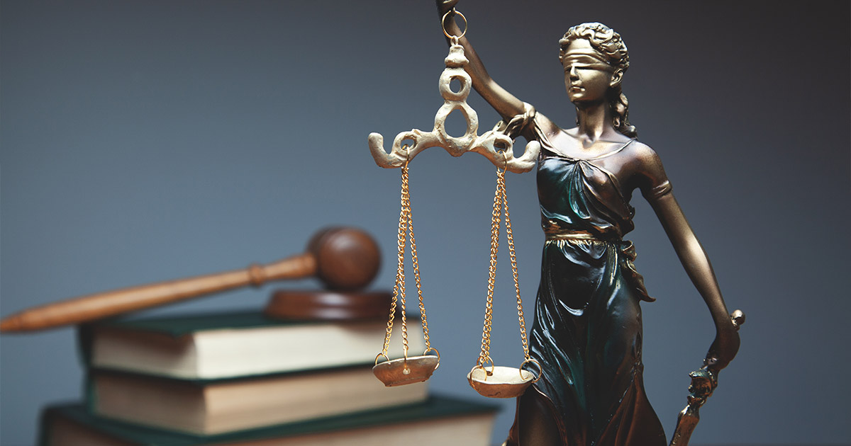 Bronze statue of Lady Justice with scales, symbolizing law, legal system, and fairness, with law books in background