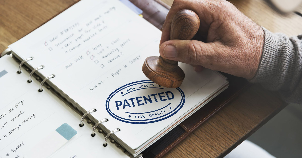 Wooden stamp marking a document with "PATENTED" stamp in blue ink, signifying high-quality intellectual property