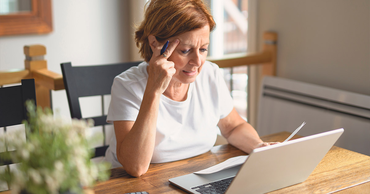 Woman with headache looking stressed while working on laptop at home office desk